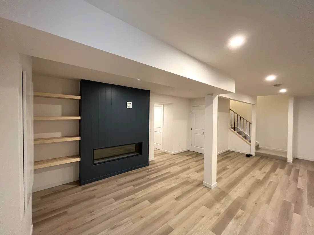 A basement with a navy shiplap fireplace wall and wood shelves