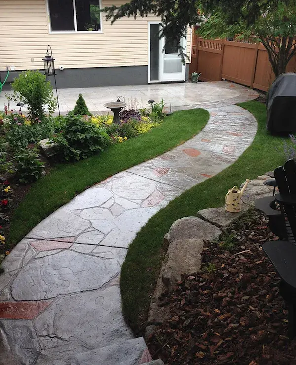 A curved two-tone stamped concrete walkway through a garden