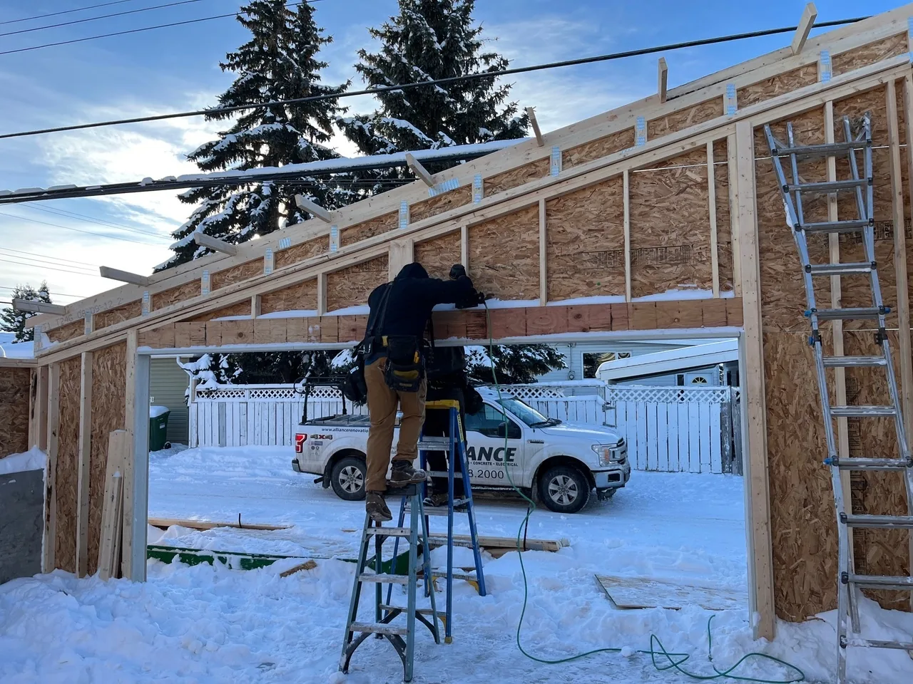 An Alliance crew framing in the snow, the company truck behind