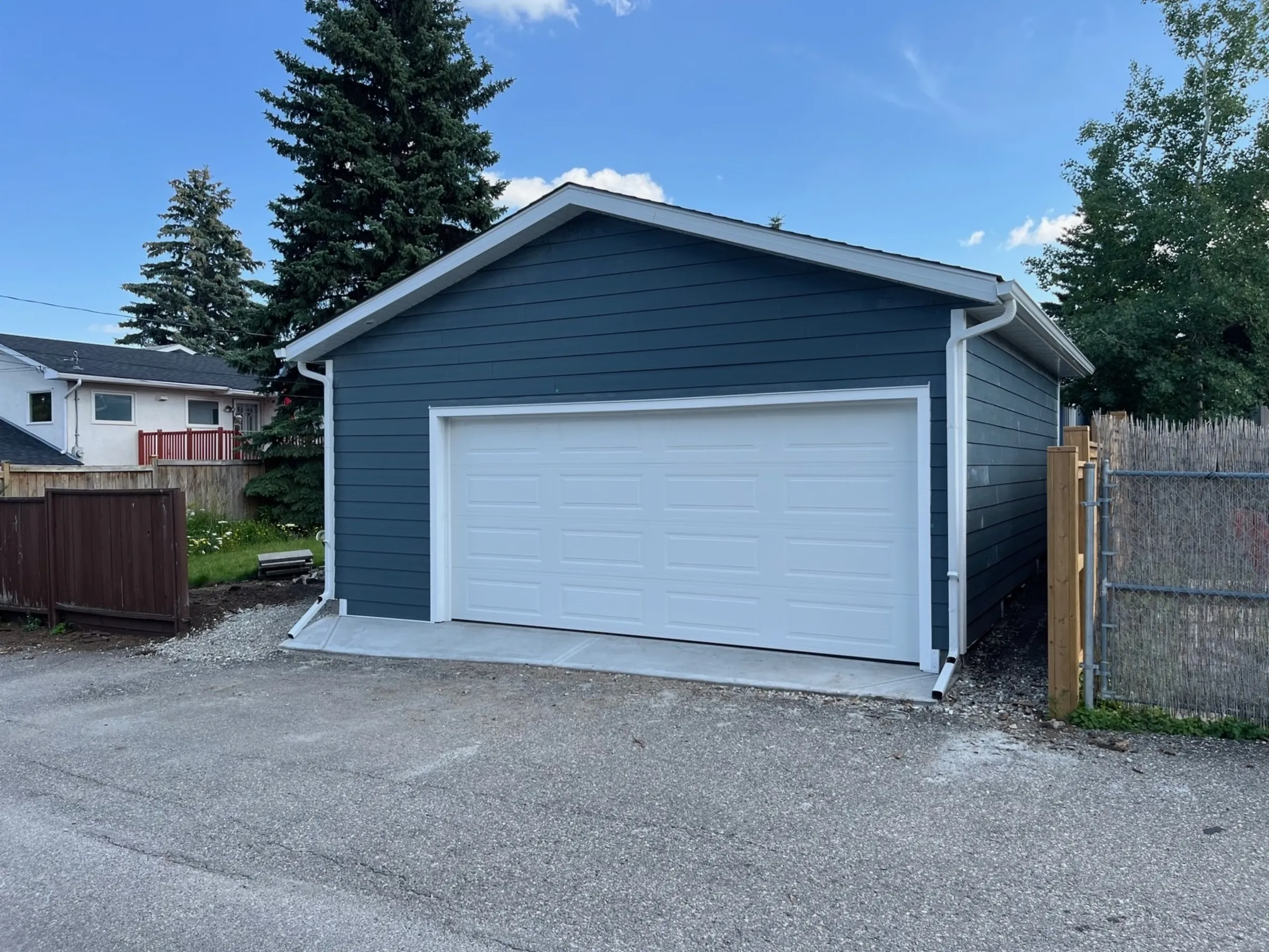 A slate blue garage with a white raised-panel door off a back lane, built by Alliance Renovations