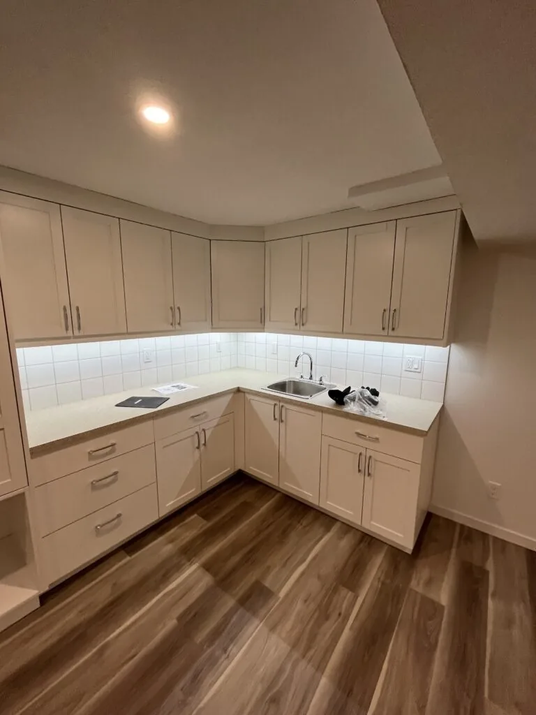 An L-shaped white shaker kitchen with under-cabinet lights in a basement suite